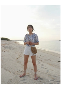 Outdoor vacation look with blue floral top and hand-woven straw crossbody bag on the beach