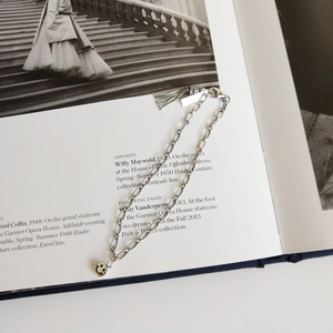Detail of S925 silver chain bracelet featuring a smile face charm and metallic tassel