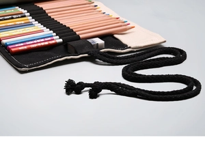 Detail of canvas roll pencil case showing texture, black woven strap, and pencils