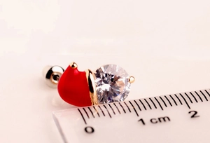 Macro shot of snowman hat earring with red oil drip and zircon next to a measuring ruler