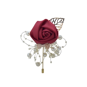Detailed close-up of burgundy artificial rose boutonniere with gold leaves and pearls
