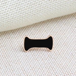 Close-up of rose gold bone-shaped brooch with black enamel inlay on fabric texture