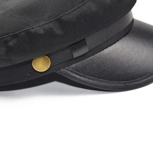 Detail of black baker boy hat with faux leather brim and gold metal button decoration