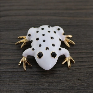 Close-up of white enamel frog brooch with gold limbs on dark wood background