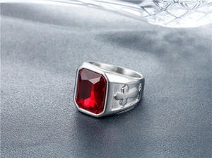 Detailed close-up of a men's signet ring with a red gemstone and embossed cross designs