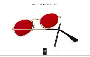 Detail view of oval sunglasses featuring red lenses and golden metal frame at 45-degree angle