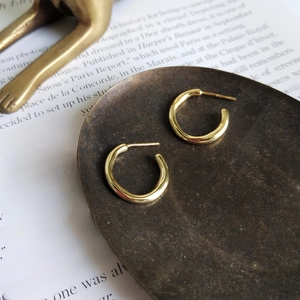 Polished gold irregular C-shape hoop earrings placed on a vintage metallic tray