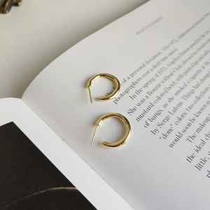 Polished 925 sterling silver hoop earrings in gold finish on minimalist book pages