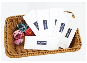 Individual wet wipes in white packaging displayed in a rustic brown basket with flowers