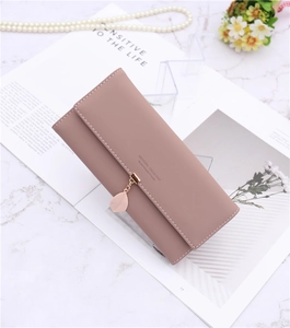 Detail of dusty pink long wallet with leaf pendant and fine stitching on marble surface