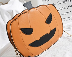 Detail of orange pumpkin crossbody bag with black face and golden chain strap