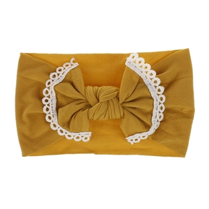 Close-up of ginger yellow nylon headband with white lace trim and bow for babies
