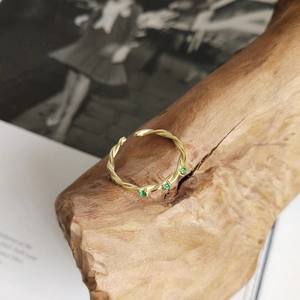 Detailed close-up of a gold twisted rope ring with three green gemstones on wood