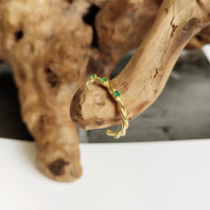 Detailed shot of a gold-plated twisted rope ring featuring four emerald green gemstones