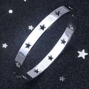 Macro detail of silver stainless steel bangle with cutout star pattern on dark background