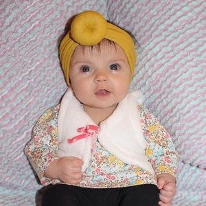Dettaglio della fascia donut in nylon giallo senape con nodo indossata da un neonato