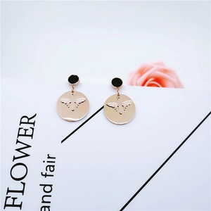 Détail de boucles d'oreilles abeille or rose avec clou noir sur carte blanche