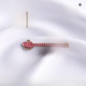 Macro shot of a pink enamel mini guitar brooch with gold metal trim on white fabric