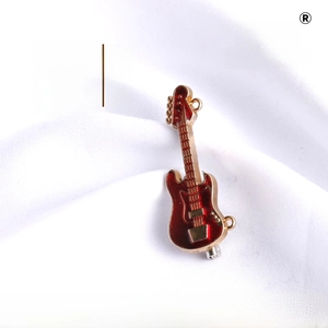 Detail of red enamel guitar brooch pin with gold metal edges on white fabric