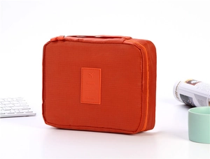 Detail view of an orange travel toiletry bag with a leather travel patch on a white desk