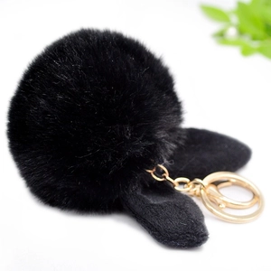 Close-up of black plush fur pompom keychain with cute rabbit ears and gold metal clasp