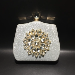 Close-up of sparkling silver evening clutch with crystal sunflower ornament and metal clasp
