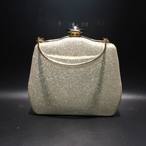 Detail of champagne gold glitter clutch featuring a large diamond clasp and metal handle