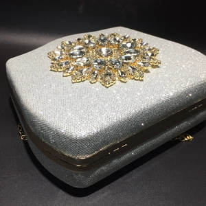 Close-up of sparkling silver evening clutch with ornate gold sunflower diamond ornament