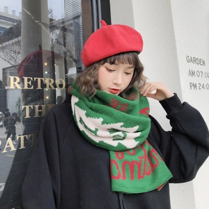 Detail of a green knitted scarf with red and white patterns worn by a female model