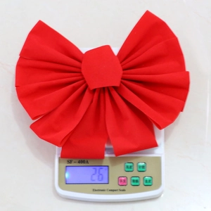 Detail view of a red velvet Christmas bow being weighed on a digital scale for size