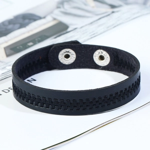 Close-up of black braided leather bracelet with snap fastener on white magazine background