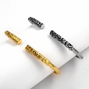 Detail of silver and gold cuff bracelets with engraved cloud patterns on white stand