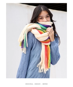 Detailed close-up of rainbow striped knit scarf with tassels on a blue cable sweater