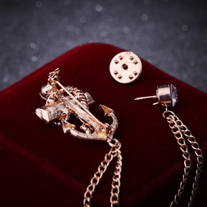Golden nautical anchor brooch with crystal studs and fringe chains on red velvet background