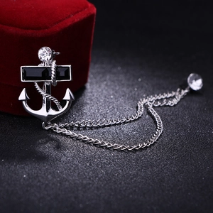 Silver anchor brooch with black gemstone and tassel chain on black textured surface