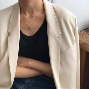 Detail of layered gold lock and key pendant necklace worn with a chic beige blazer