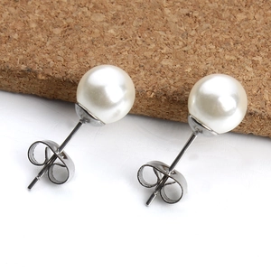 Detailed close-up of white pearl stud earrings with polished steel backings on dual-tone surface