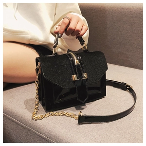 Detail of black contrast texture handbag with gold metal handle and chain strap on sofa