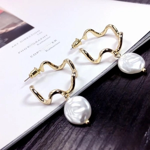 Elegant gold wave earrings with baroque pearl charms on vintage magazine background
