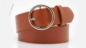 Detail of camel leather belt featuring a large circular golden buckle for jeans