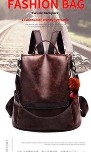 Close-up of brown pebbled leather backpack featuring a side zipper and plush pompom charm