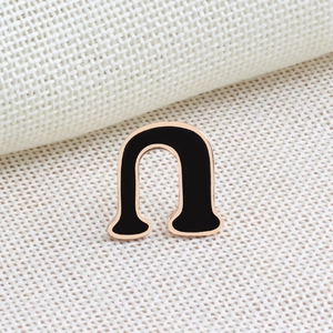 Macro shot of gold-plated U-shaped brooch with black enamel inlay on white fabric