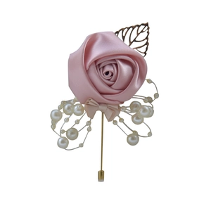 Detailed close-up of a pink satin rose brooch with white pearls and a golden leaf accent