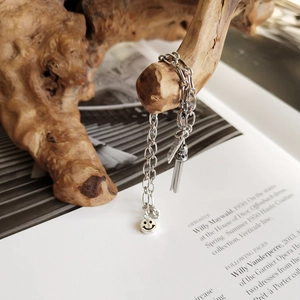 Elegant S925 silver bracelet featuring smiley face and tassel charms on wood background