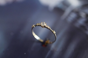 Macro shot of gold six-prong setting ring with tiny diamonds on a dark blue background