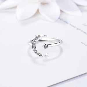 Silver open moon and star ring with sparkling stones on textured white background