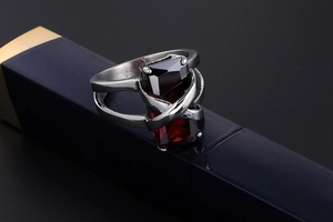 Detailed close-up of a silver cross ring with a rectangular red ruby on a dark background