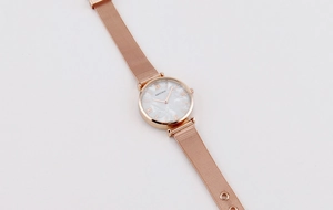 Macro view of rose gold mesh strap and white marble dial with Roman numerals