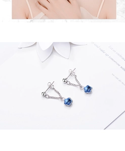 Detail of silver stud earrings with blue flower crystal pendants on a floral paper