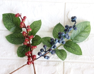Close-up of red and blue artificial blueberries with realistic green leaves and veins